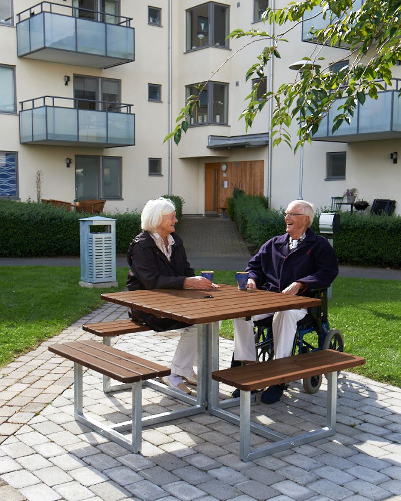 Two seniors sitting on a Skagen picnic table. One of them in a wheelchair..